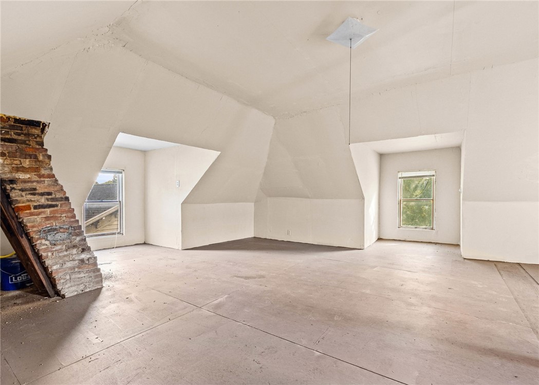 Unfinished attic room with sloped ceilings, two windows, and exposed brickwork.