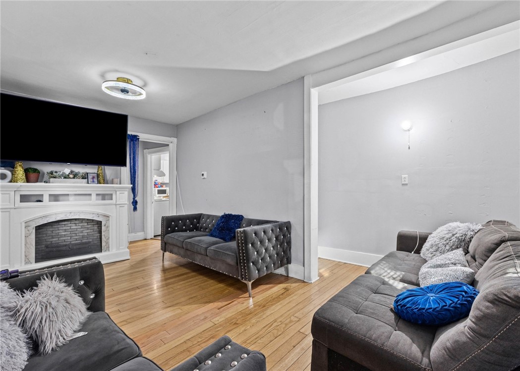 Living room with gray tufted sofas, hardwood floors, white fireplace, and wall-mounted television.