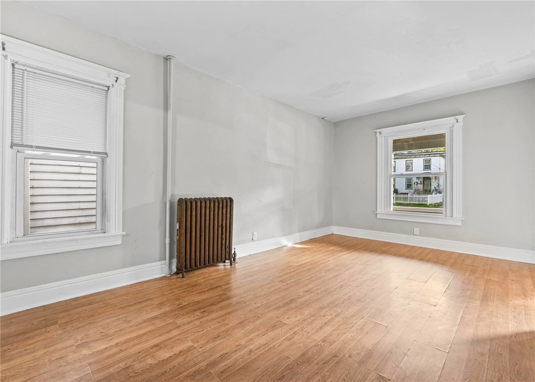 Vacant room with hardwood floors, ornate white-trimmed windows, and a vintage radiator.