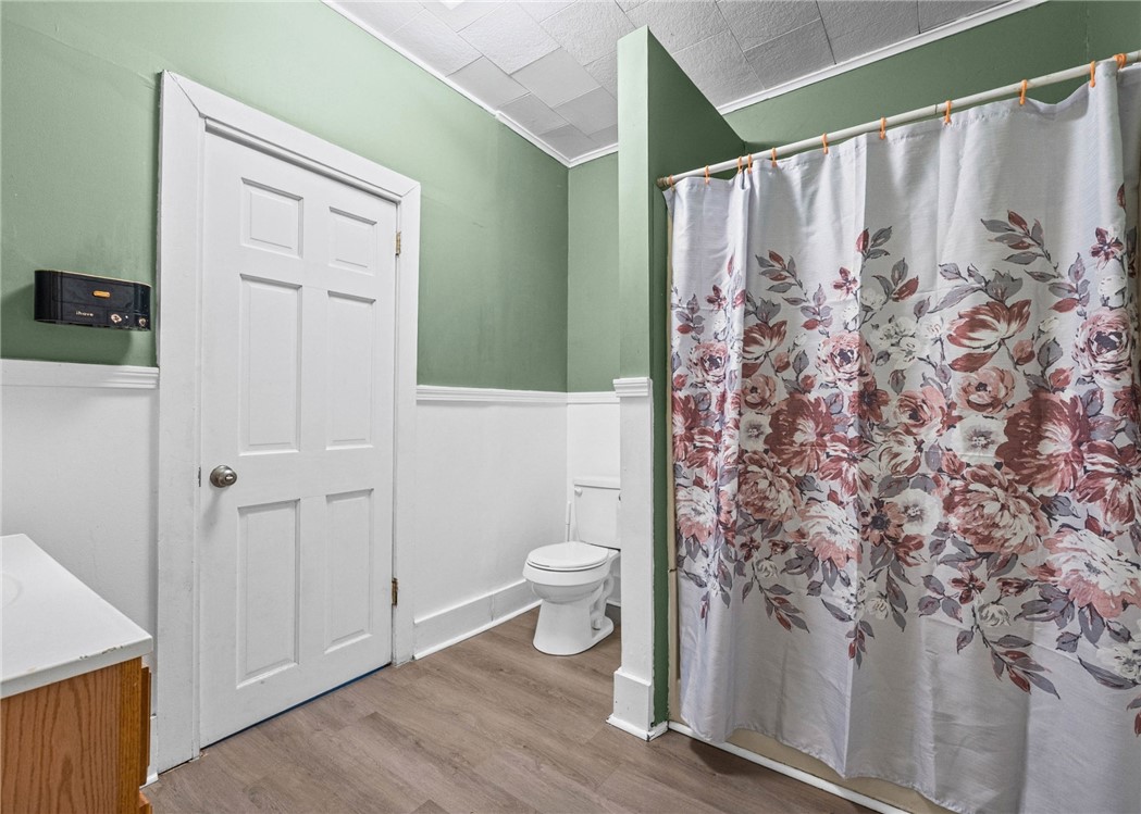 Bathroom with green walls, white wainscoting, and a floral shower curtain.