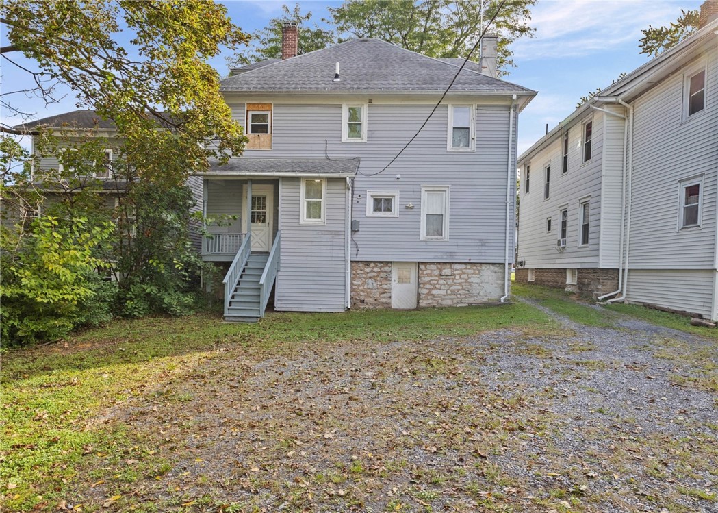 Rear exterior of a gray-sided house with a stone foundation, porch stairs, and gravel driveway.