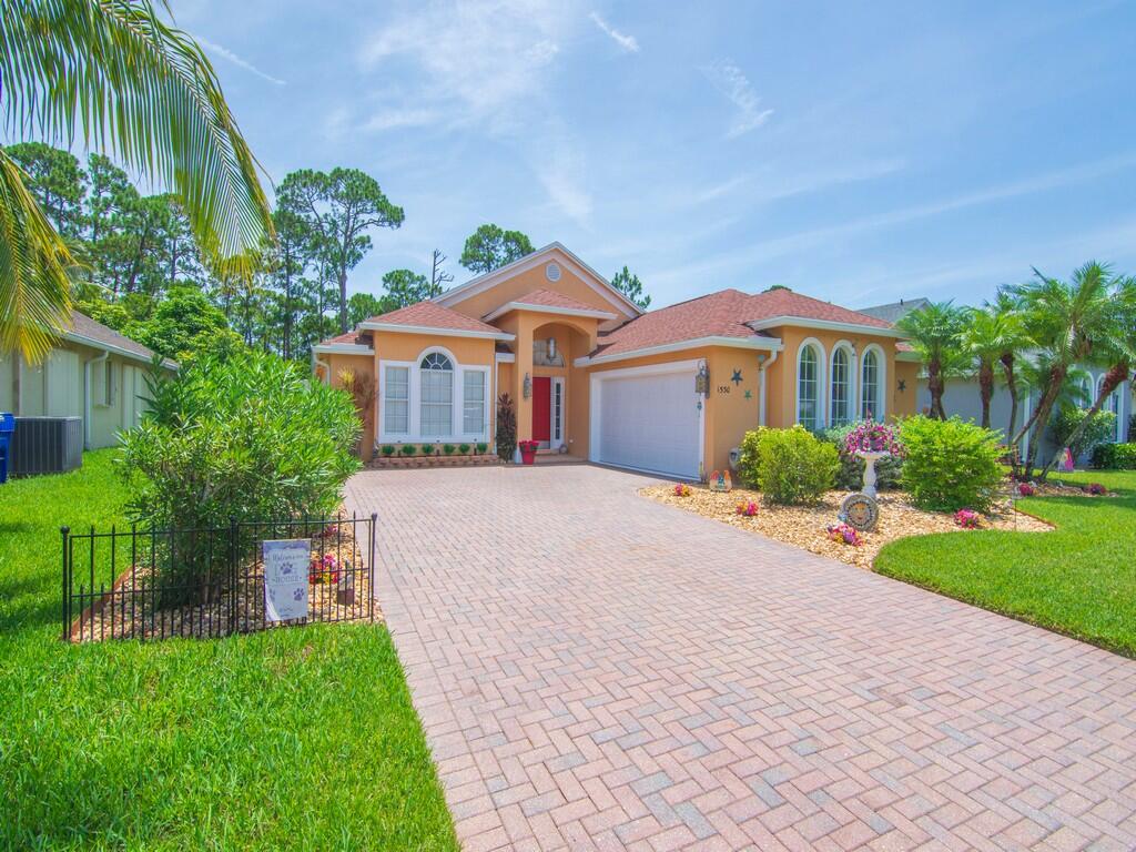 Peach stucco home with arched windows, red tile roof, and broad brick-paver driveway.