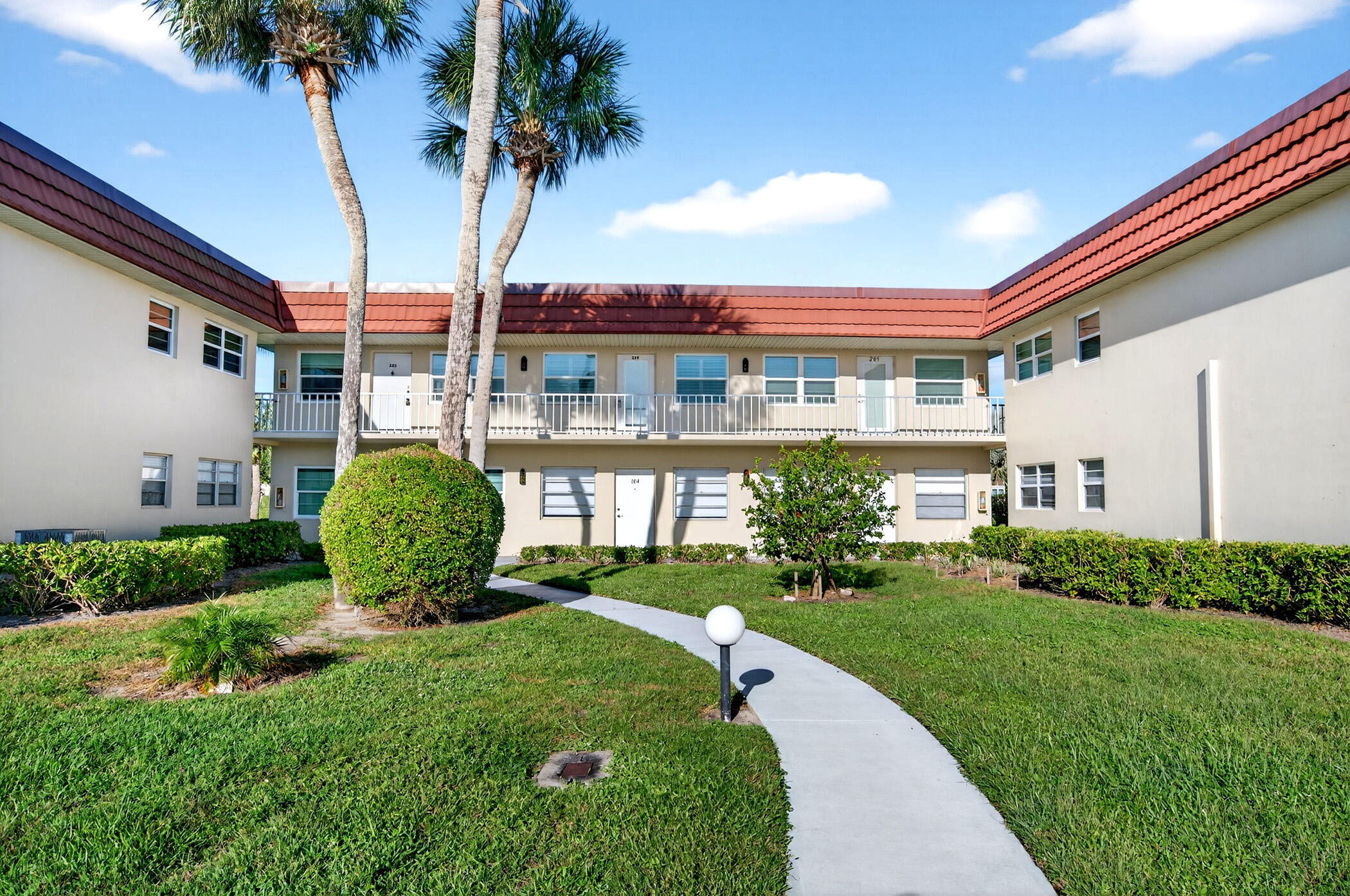 Two-story condominium buildings surround a landscaped courtyard with palms and a curving walkway.