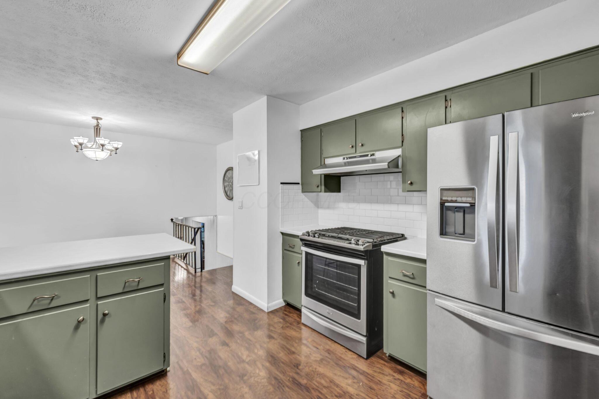Kitchen with sage-green cabinets, stainless appliances, white subway-tile backsplash, and wood-look floors.