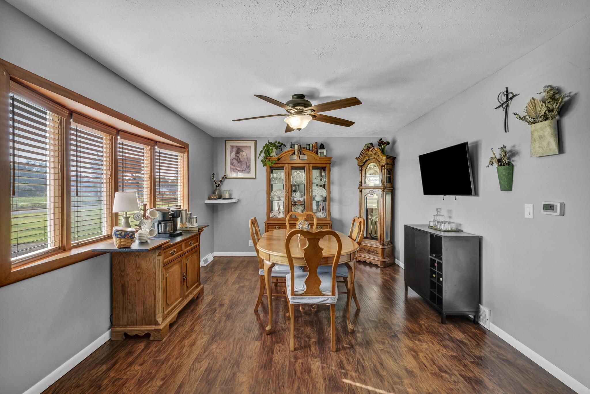 Dining room with a wooden table, large windows, china cabinet, and grandfather clock.
