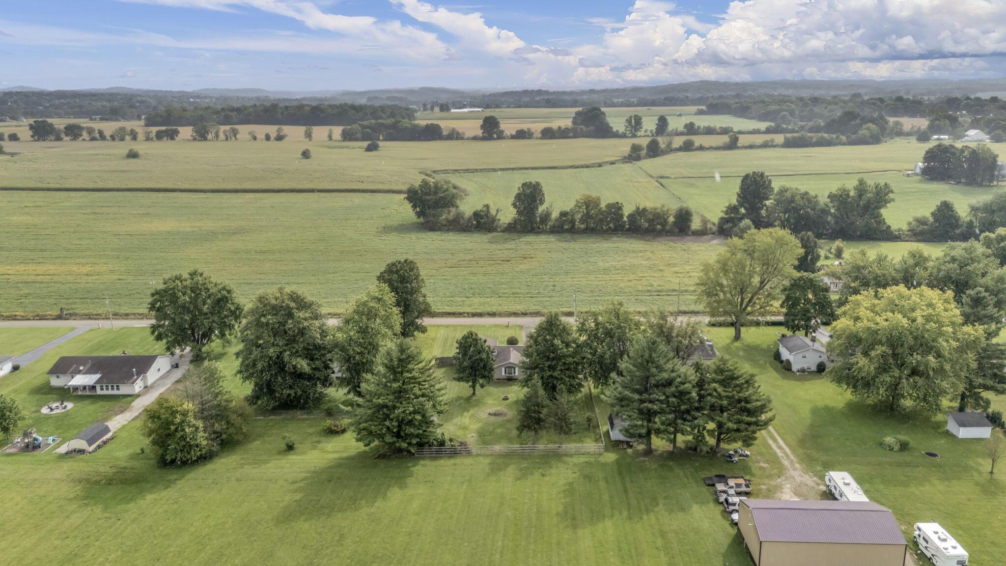 Aerial view of a rural property with a broad lawn, homes, outbuildings, and surrounding fields.