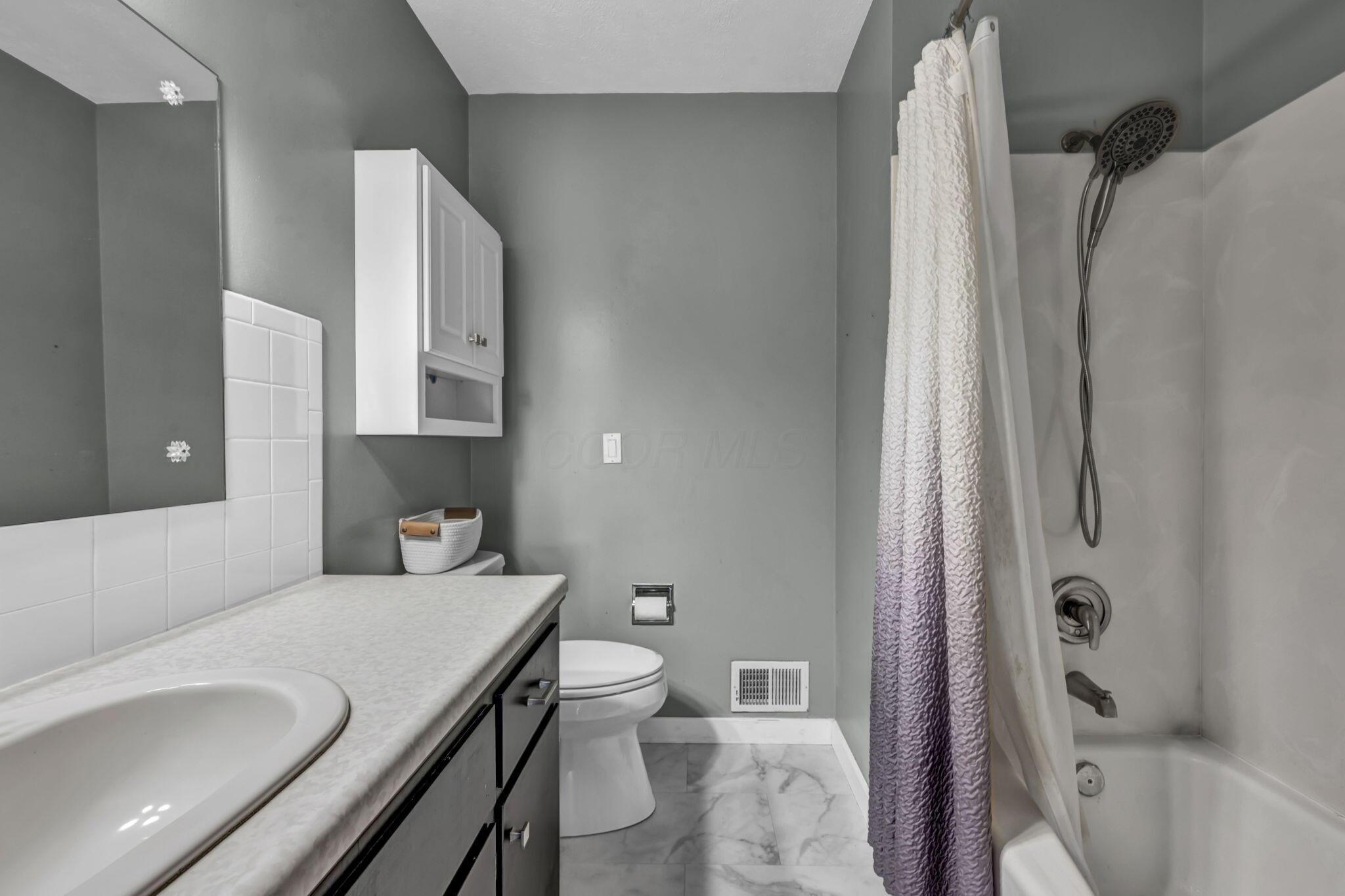 Bathroom with a white vanity, toilet, and tub-shower behind a textured curtain.