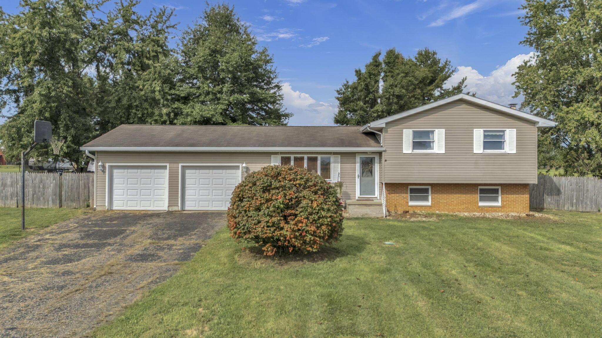 Tan split-level home with a brick lower facade, two-car garage, and basketball hoop by the driveway.