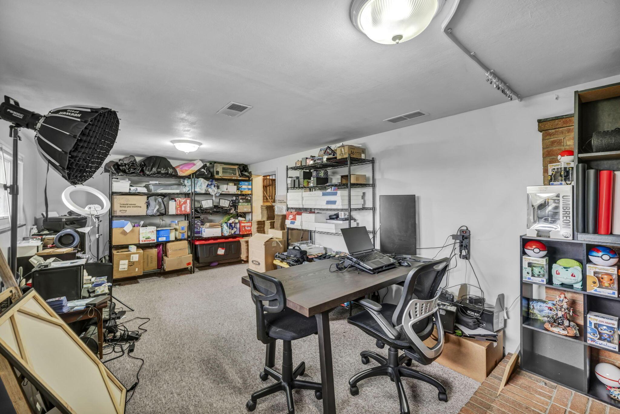 Carpeted office and storage room with a desk, shelving, photography equipment, and collectibles.
