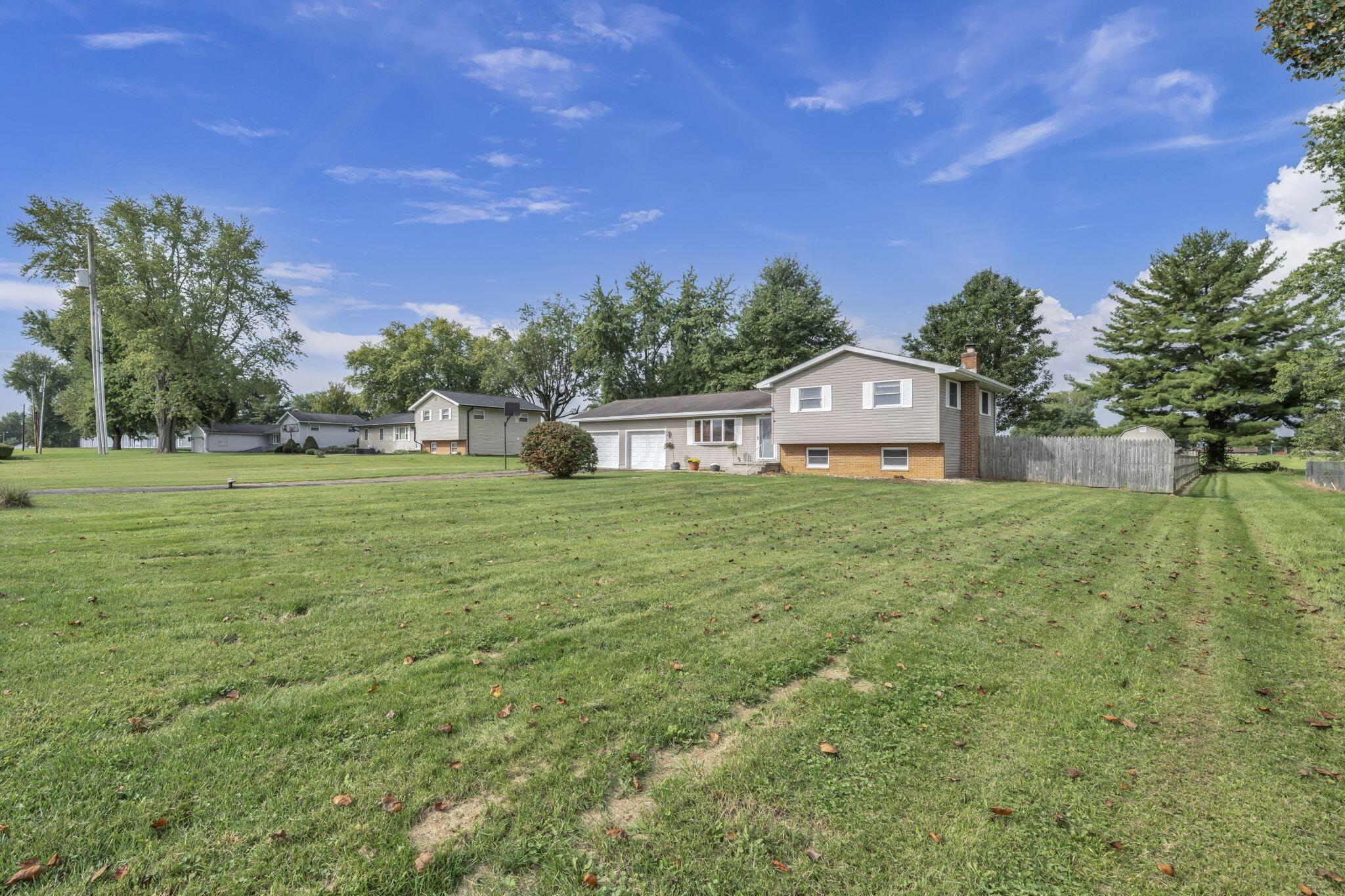 Split-level home with an attached garage, broad lawn, and wooden privacy fence.
