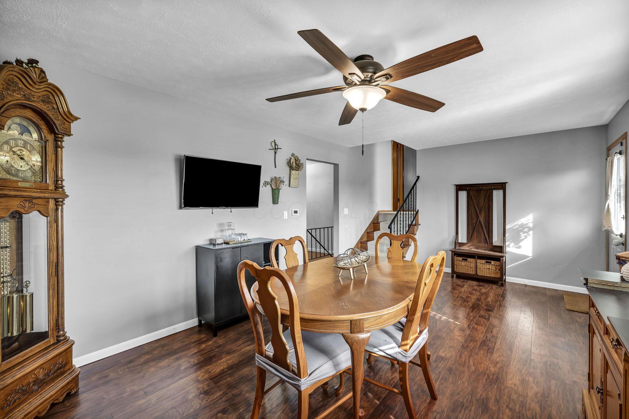 Dining room with a wooden table, grandfather clock, ceiling fan, and stairs.