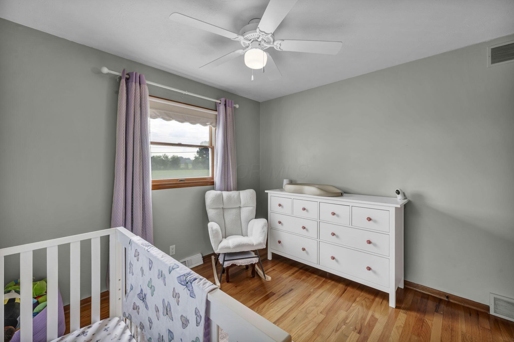 Nursery with a white crib, butterfly bedding, dresser, rocking chair and lavender curtains.