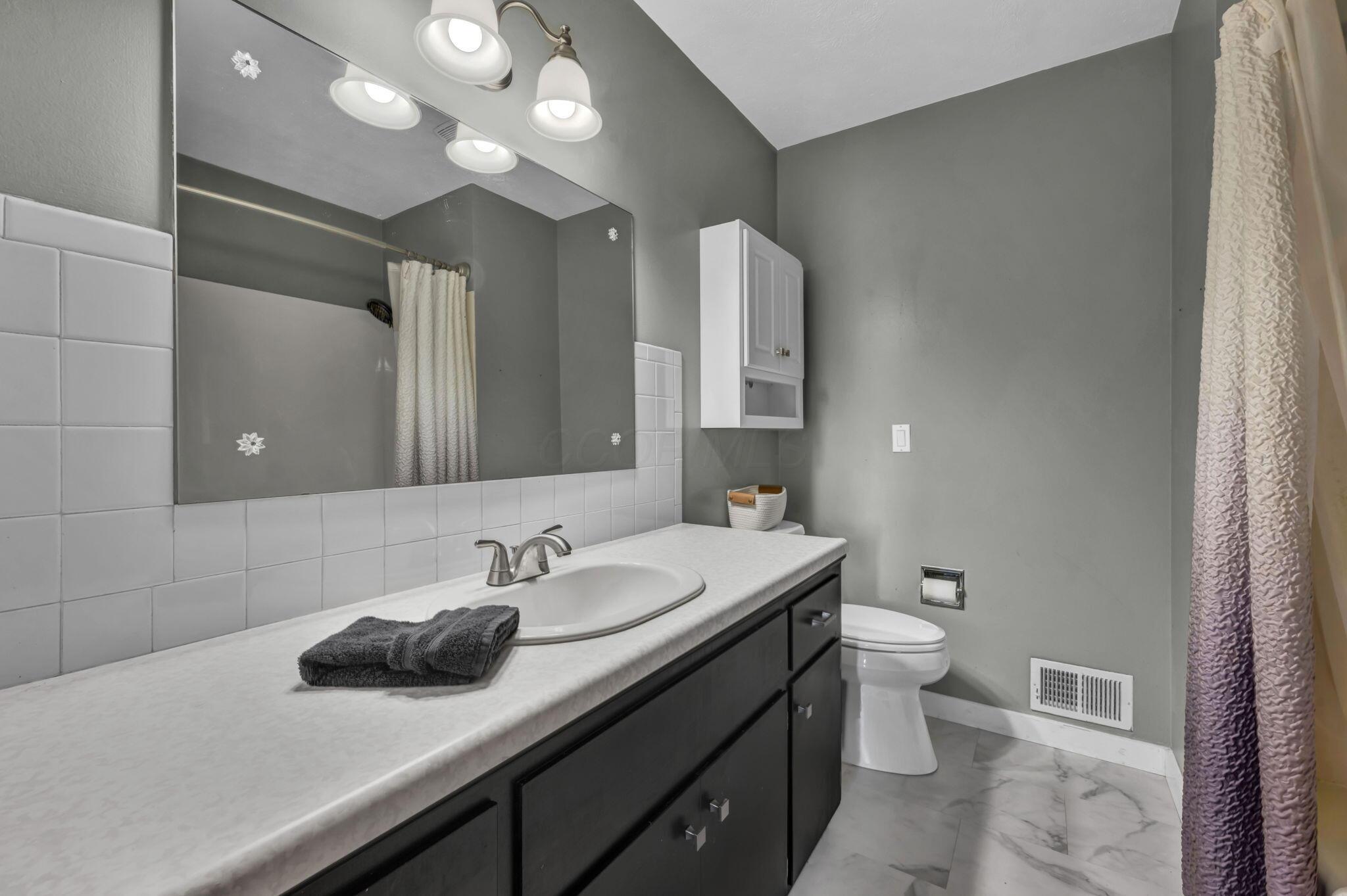 Bathroom with a long dark vanity, large mirror, tiled backsplash, and curtained tub or shower.