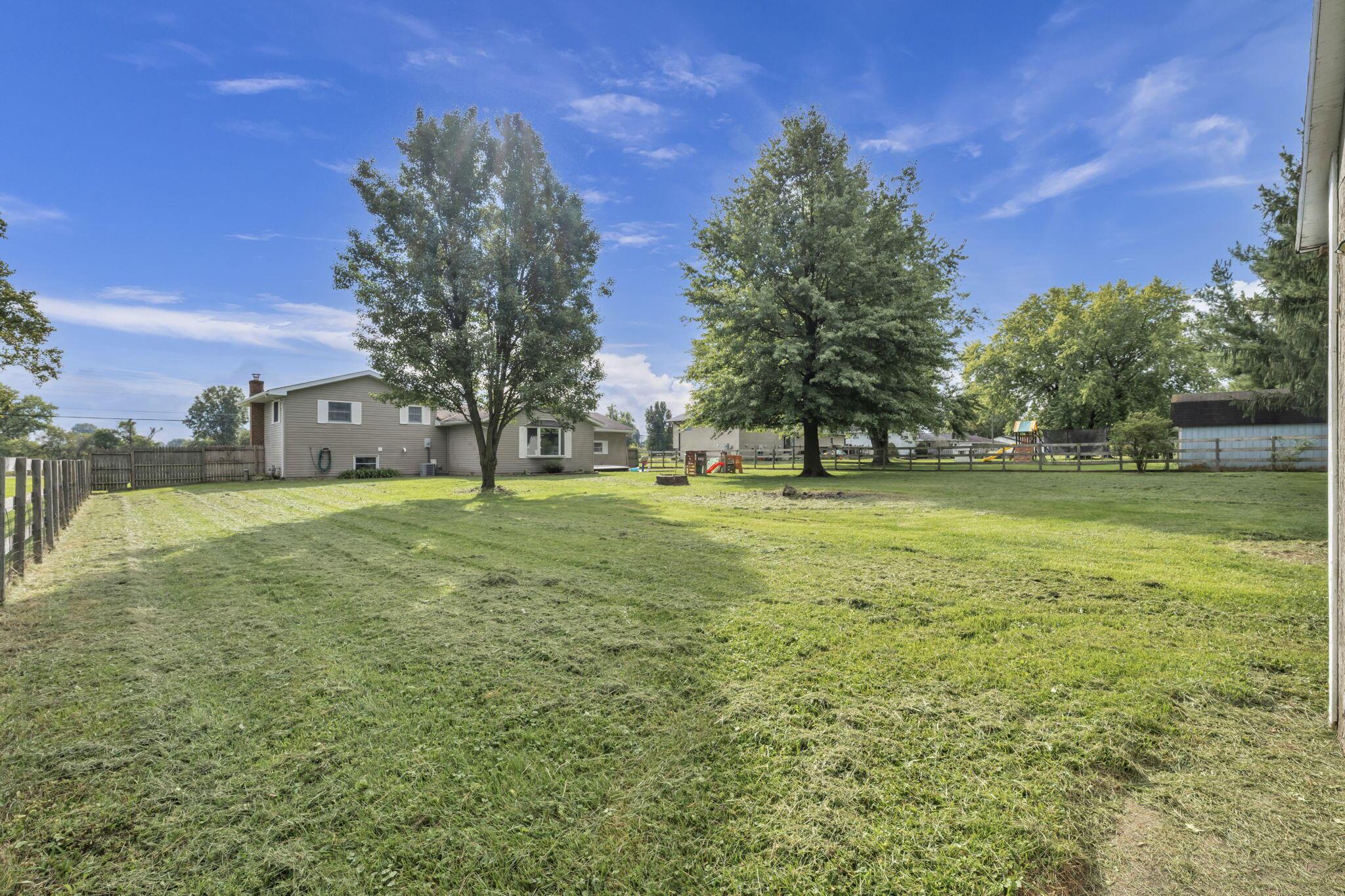 Spacious fenced backyard with mature trees, a children's playset, and the rear of the house.