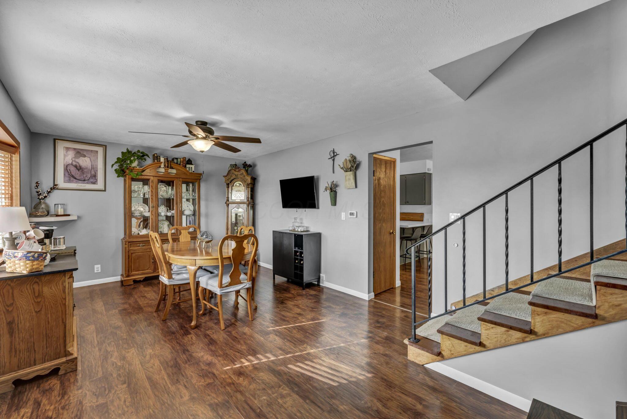 Dining area with a wooden table and china cabinet beside a staircase with a black railing.