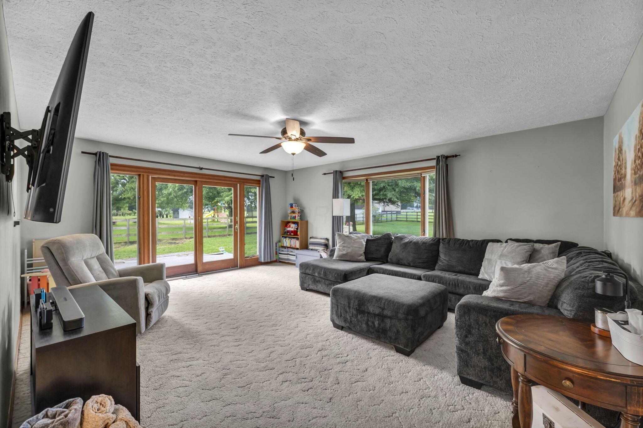 Living room with a dark sectional, ceiling fan, and sliding glass doors overlooking a fenced yard.