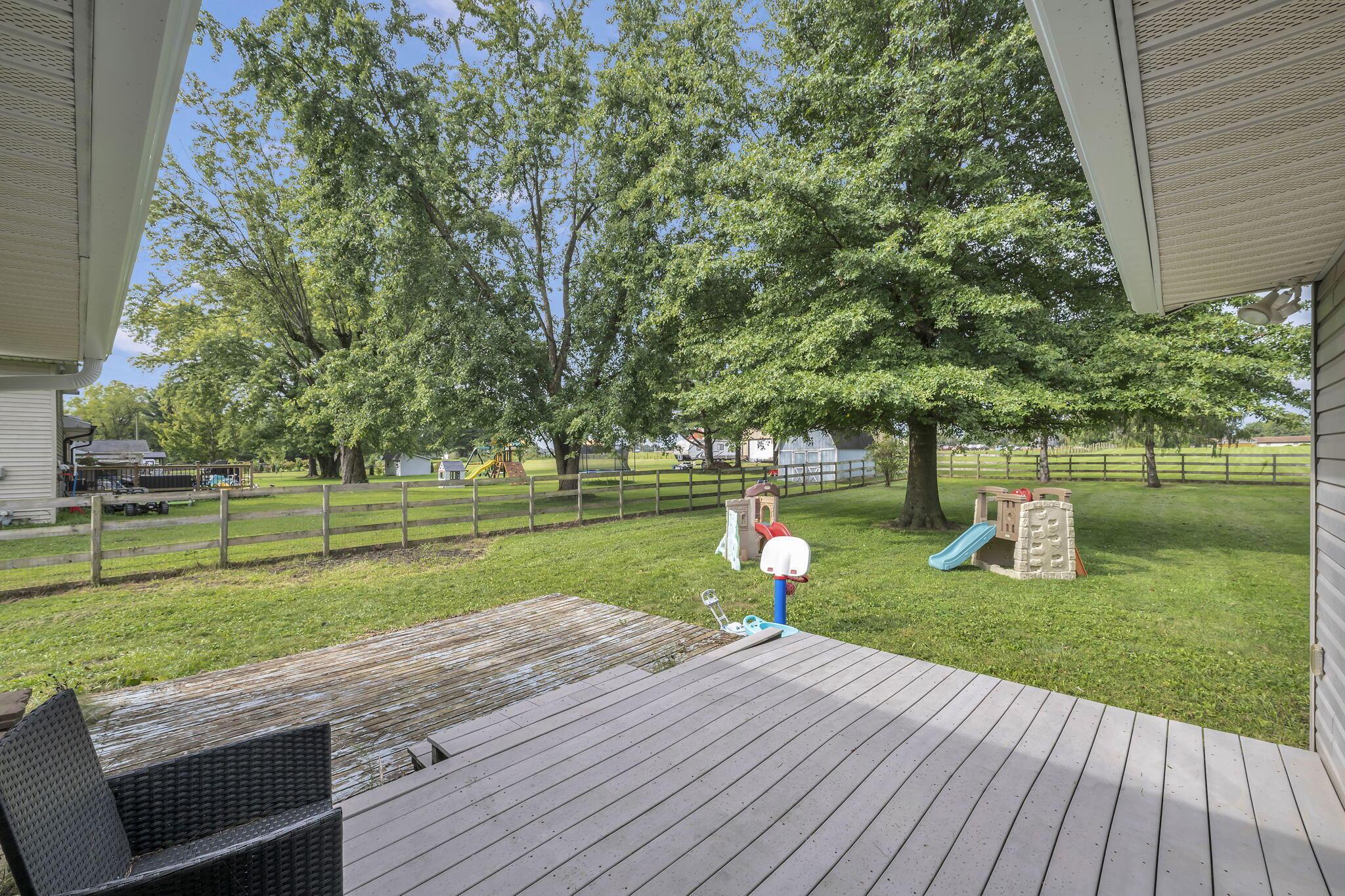Covered rear deck overlooking a fenced, tree-shaded backyard with two playsets.