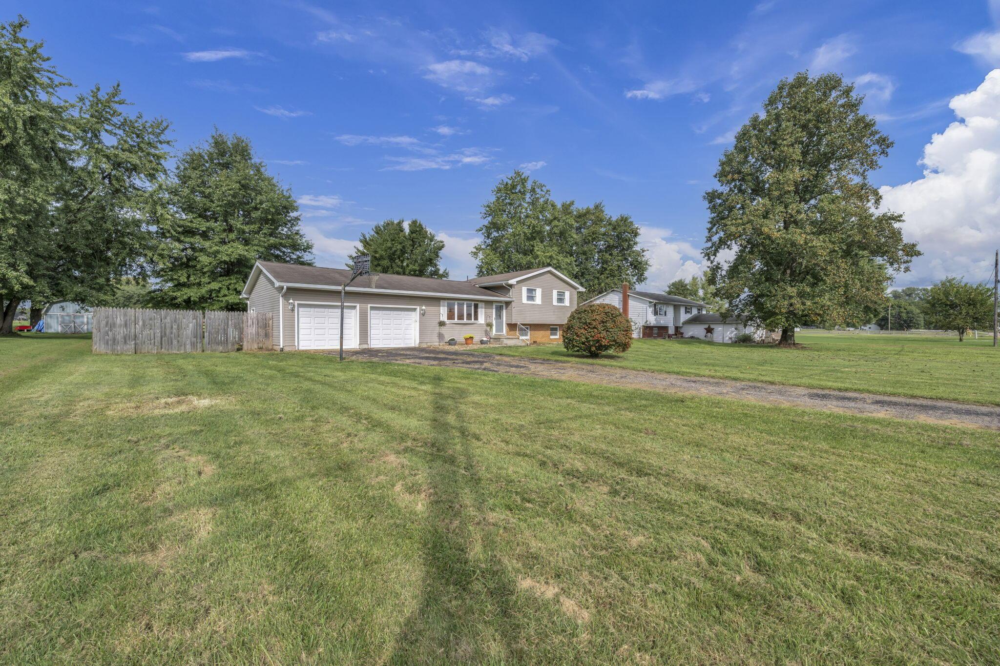 Tan split-level home with two garage doors, a gravel driveway, and a broad grassy yard.