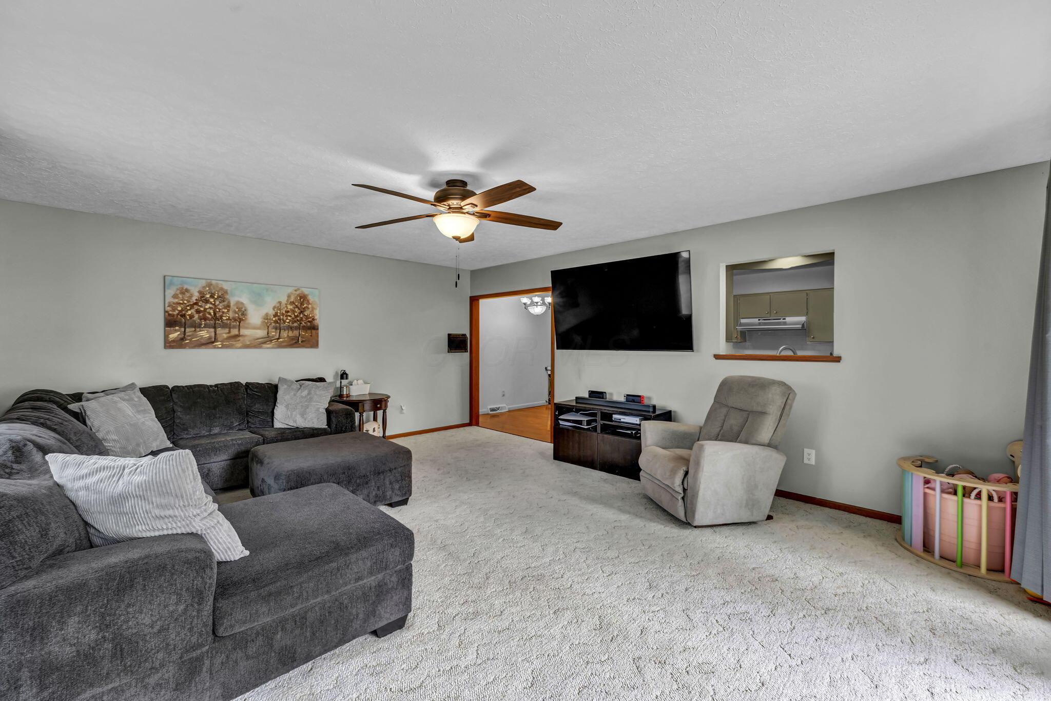 Living room with a gray sectional, recliner, wall-mounted television, and kitchen pass-through.