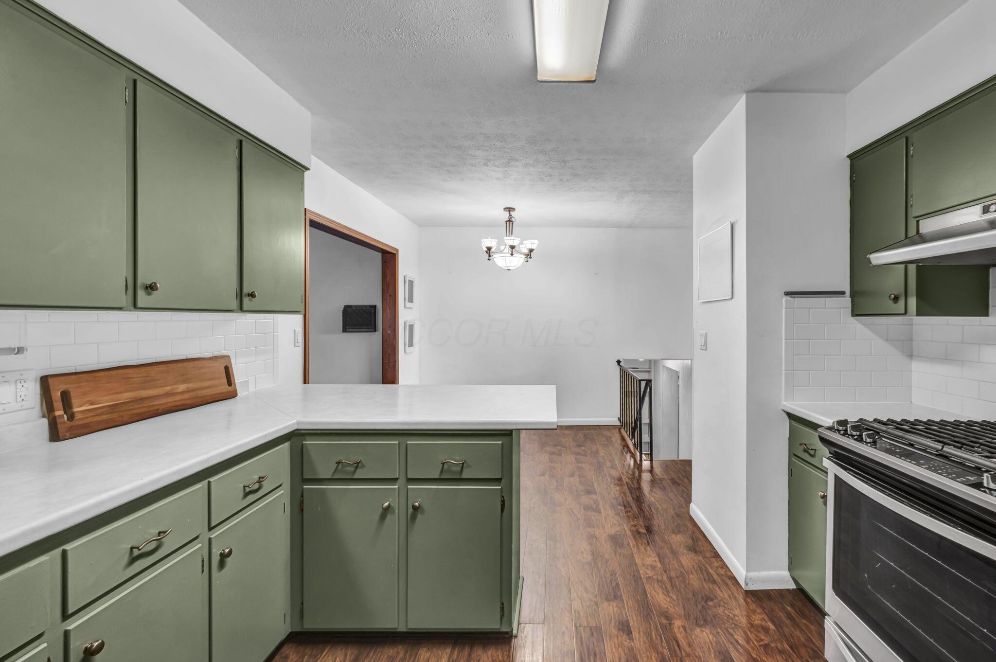 Kitchen with sage-green cabinets, white counters, gas range, and wood-look flooring.