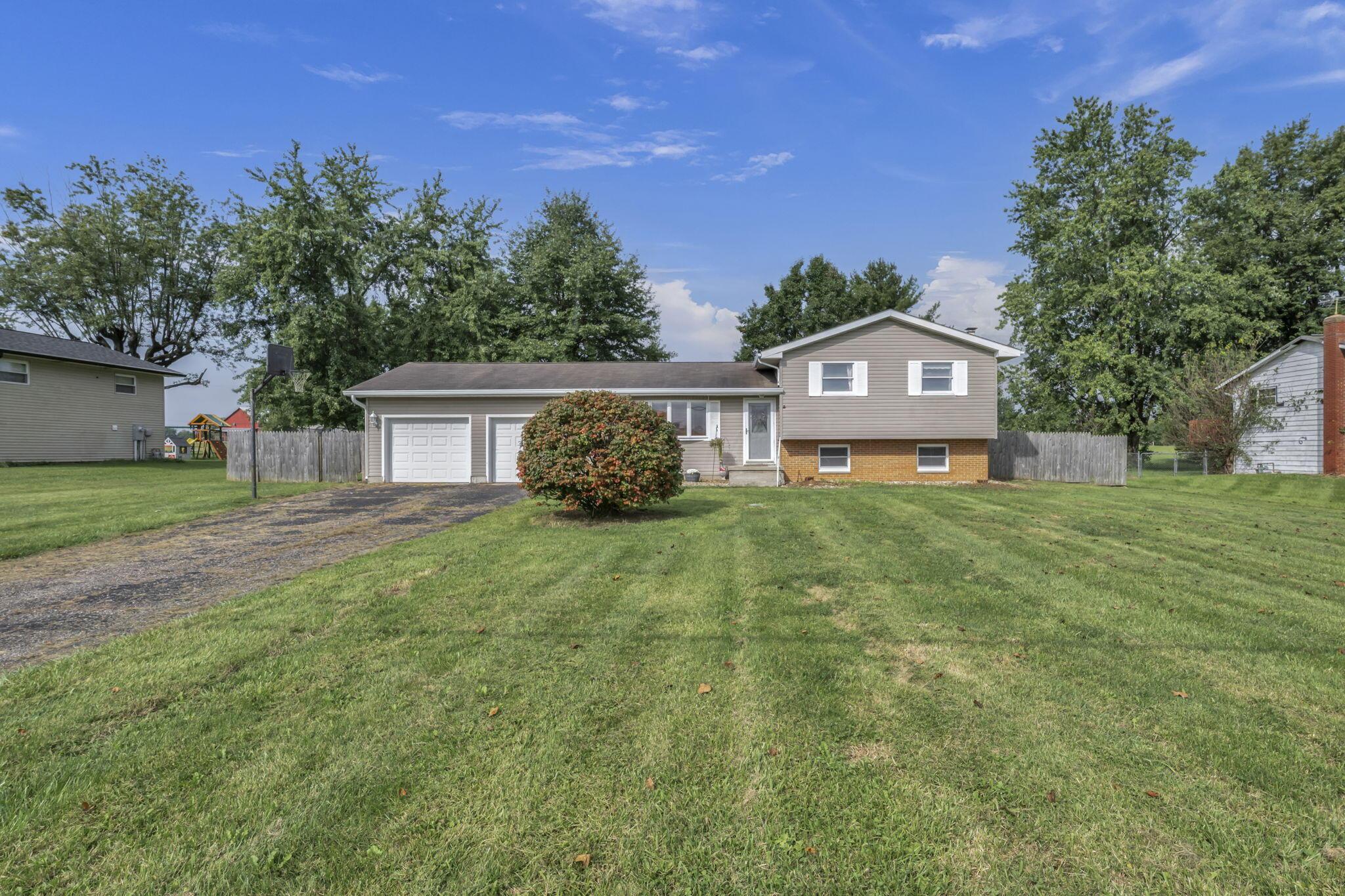 Beige split-level home with a two-car garage, brick lower facade, and a broad front lawn.
