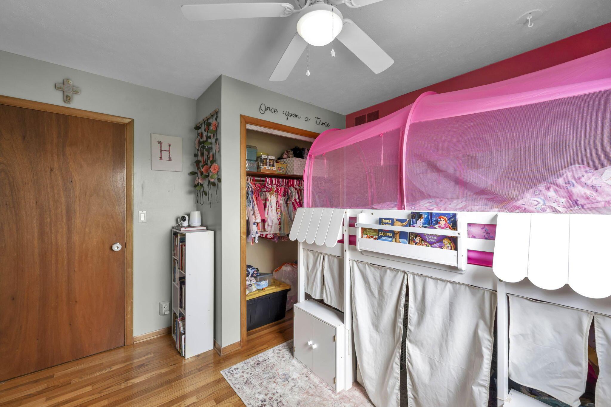 Child’s bedroom with a white canopy bed, pink netting, and a closet filled with children’s clothes.
