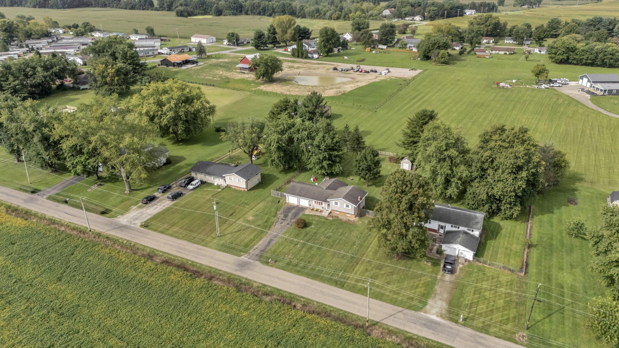 Aerial view of rural homes and fields, with a small pond and road in the foreground.