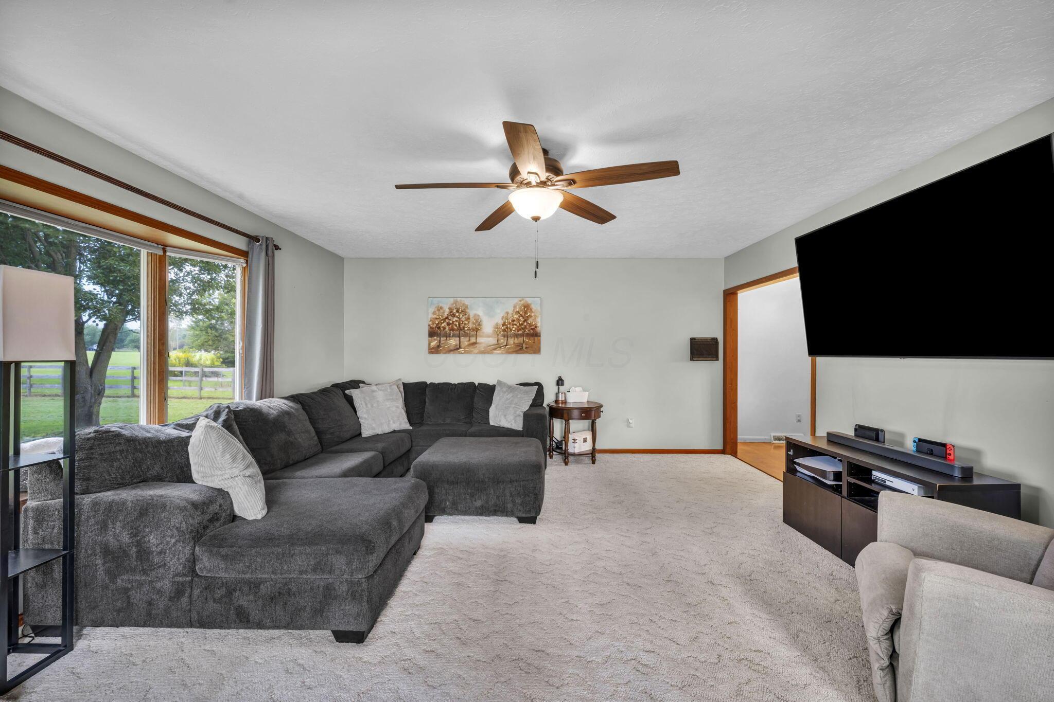 Living room with a dark gray sectional, large yard-facing windows, and a ceiling fan.