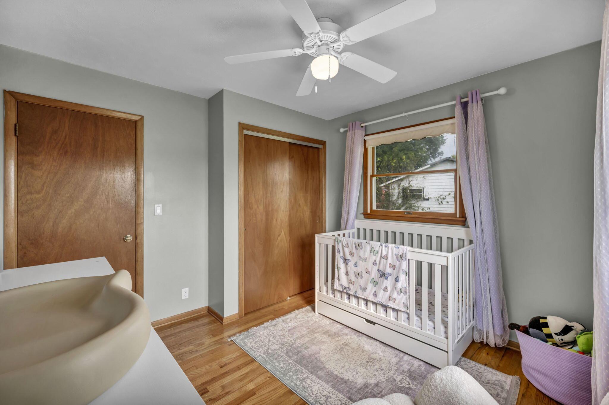 Nursery with a white crib beneath a wood-trimmed window and purple curtains.