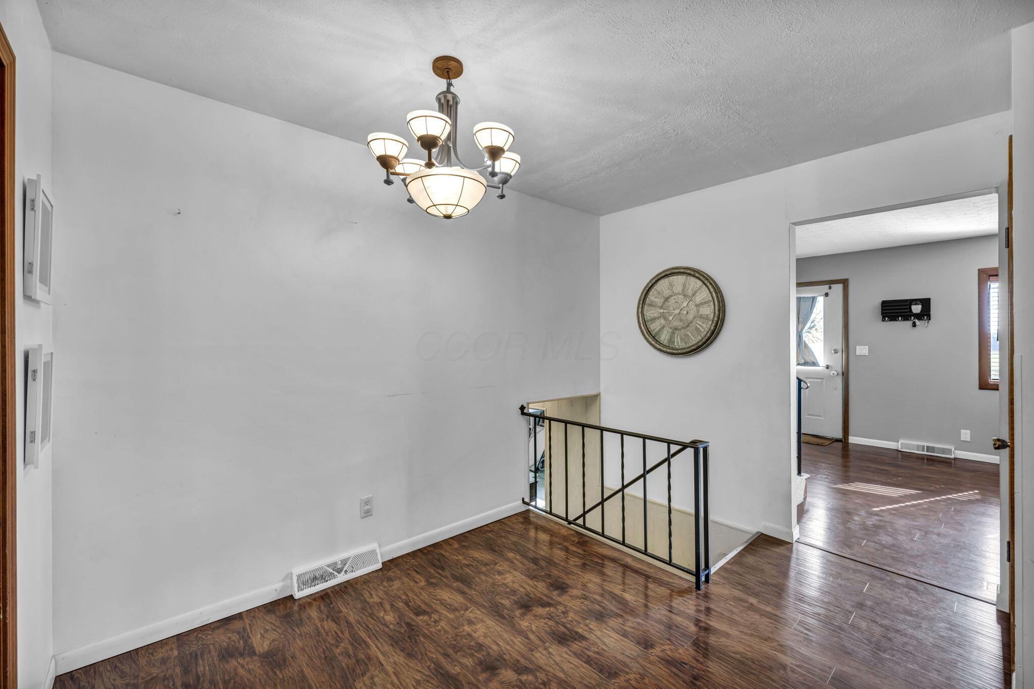 Entry hall with dark wood floors, a chandelier, and a railing around the stair opening.