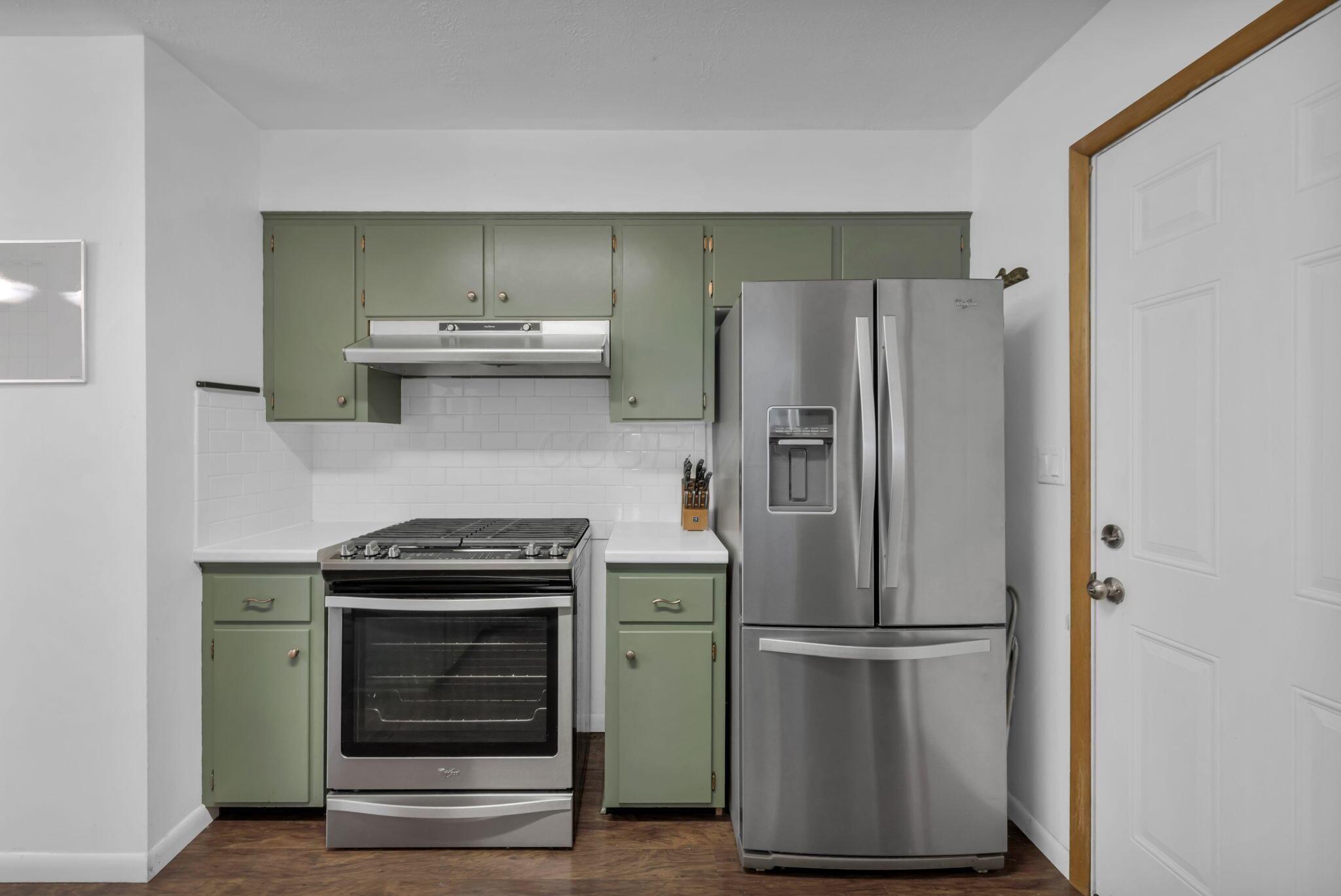 Kitchen with sage-green cabinets, white tile backsplash, and stainless-steel appliances.