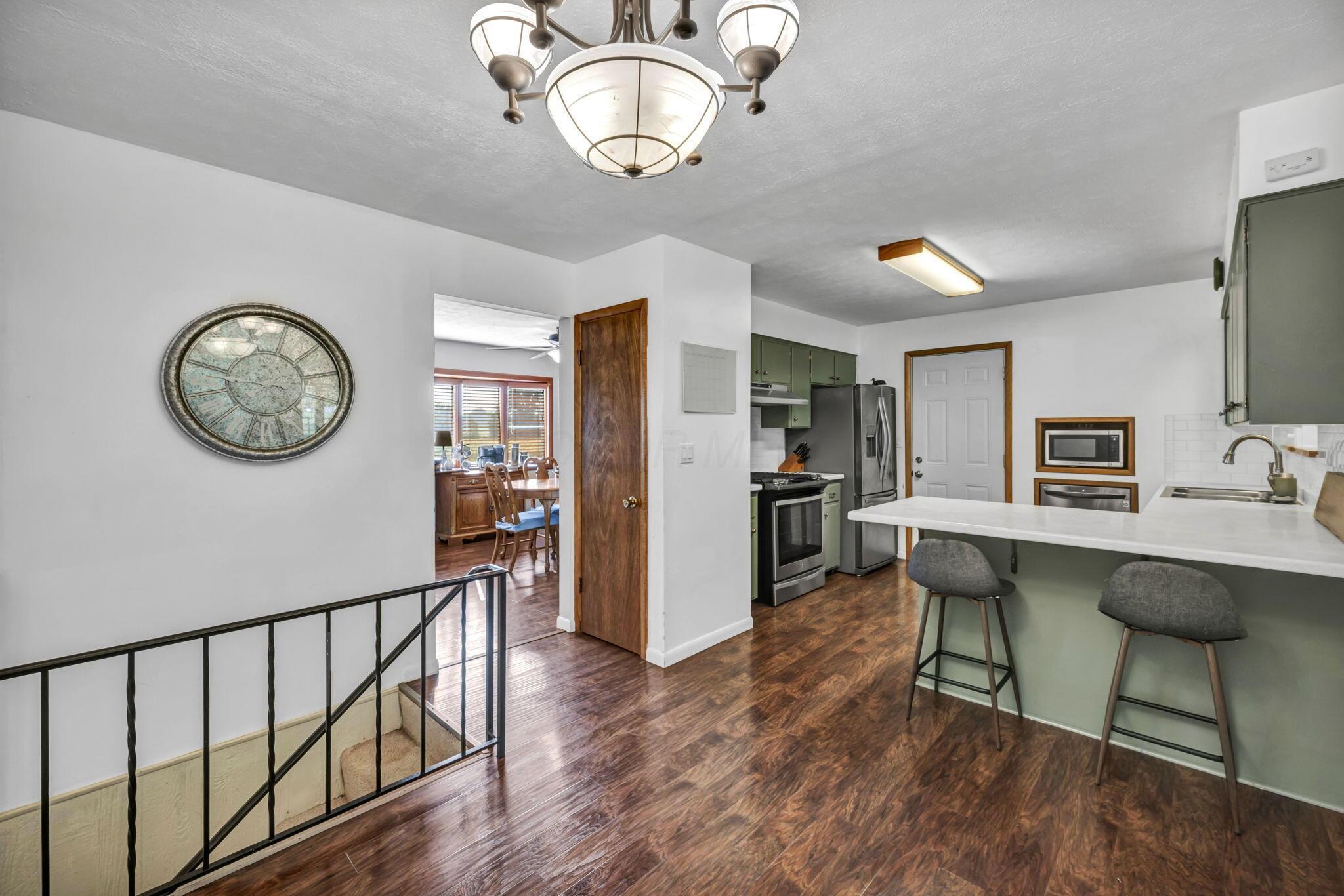 Kitchen with sage-green cabinets, stainless appliances, and a white island with two stools.