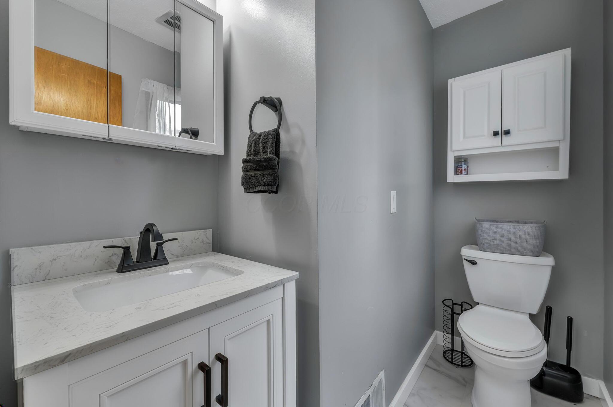 Bathroom with a marble-look vanity, black faucet, mirrored medicine cabinet, and white toilet.
