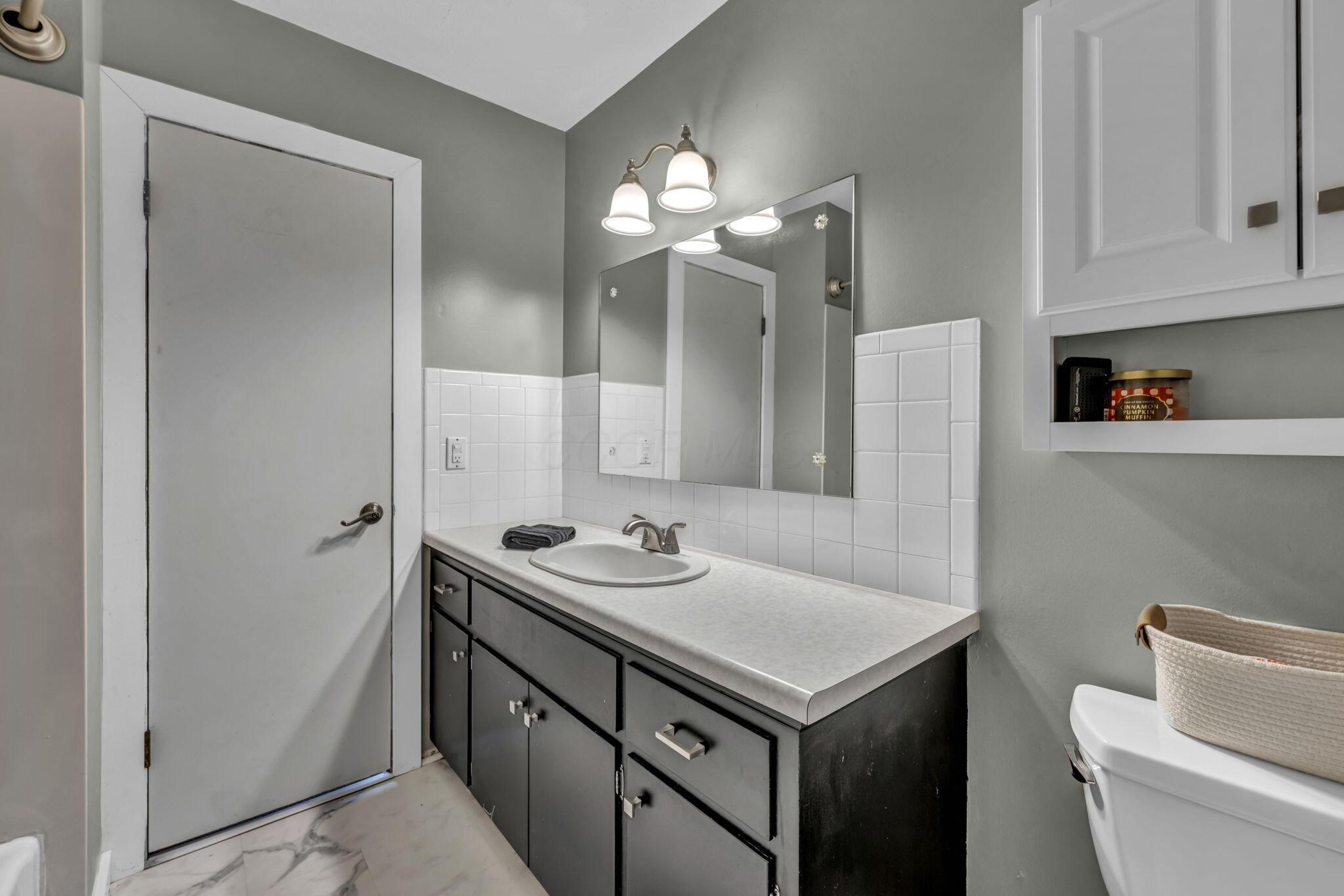 Bathroom vanity with gray cabinets, an oval sink, large mirror, and white tile backsplash.