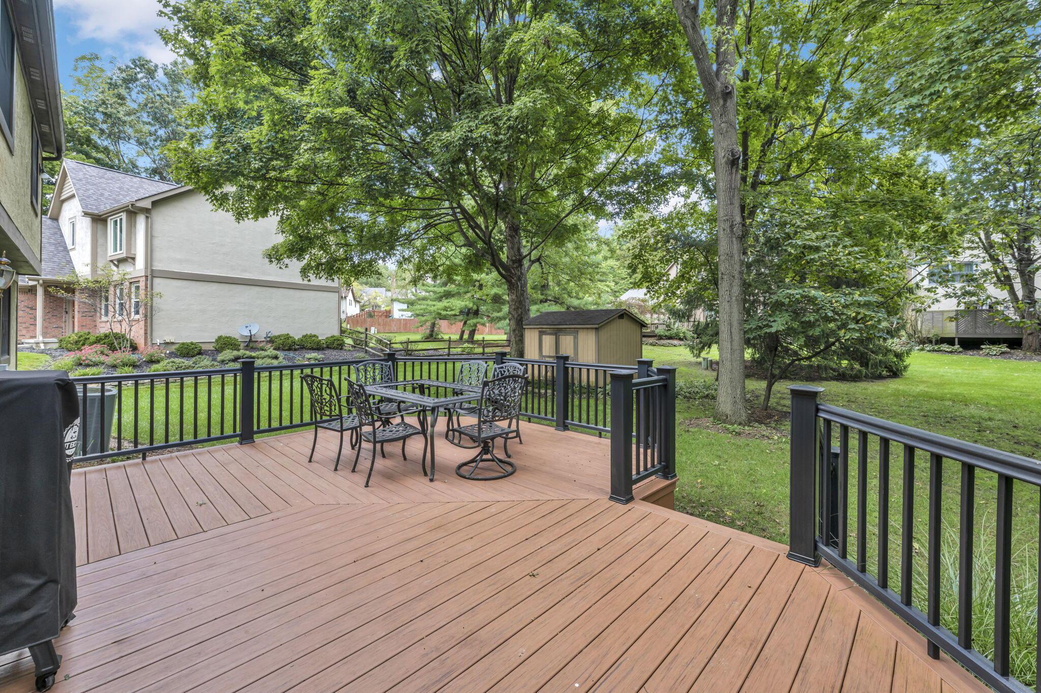 Backyard deck with black railings, outdoor dining set, mature trees, and lawn.