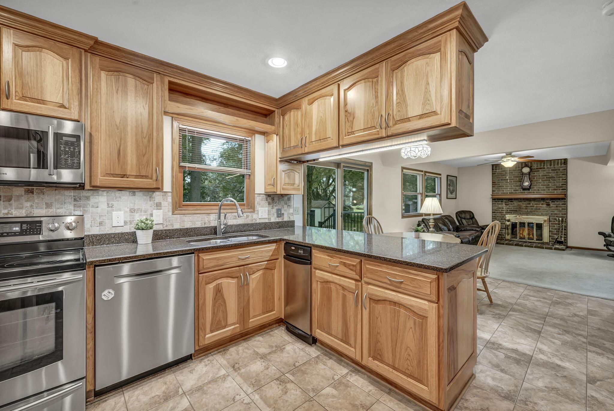 Kitchen with honey-toned wood cabinets, granite counters, stainless steel appliances, and a peninsula opening to the living room.