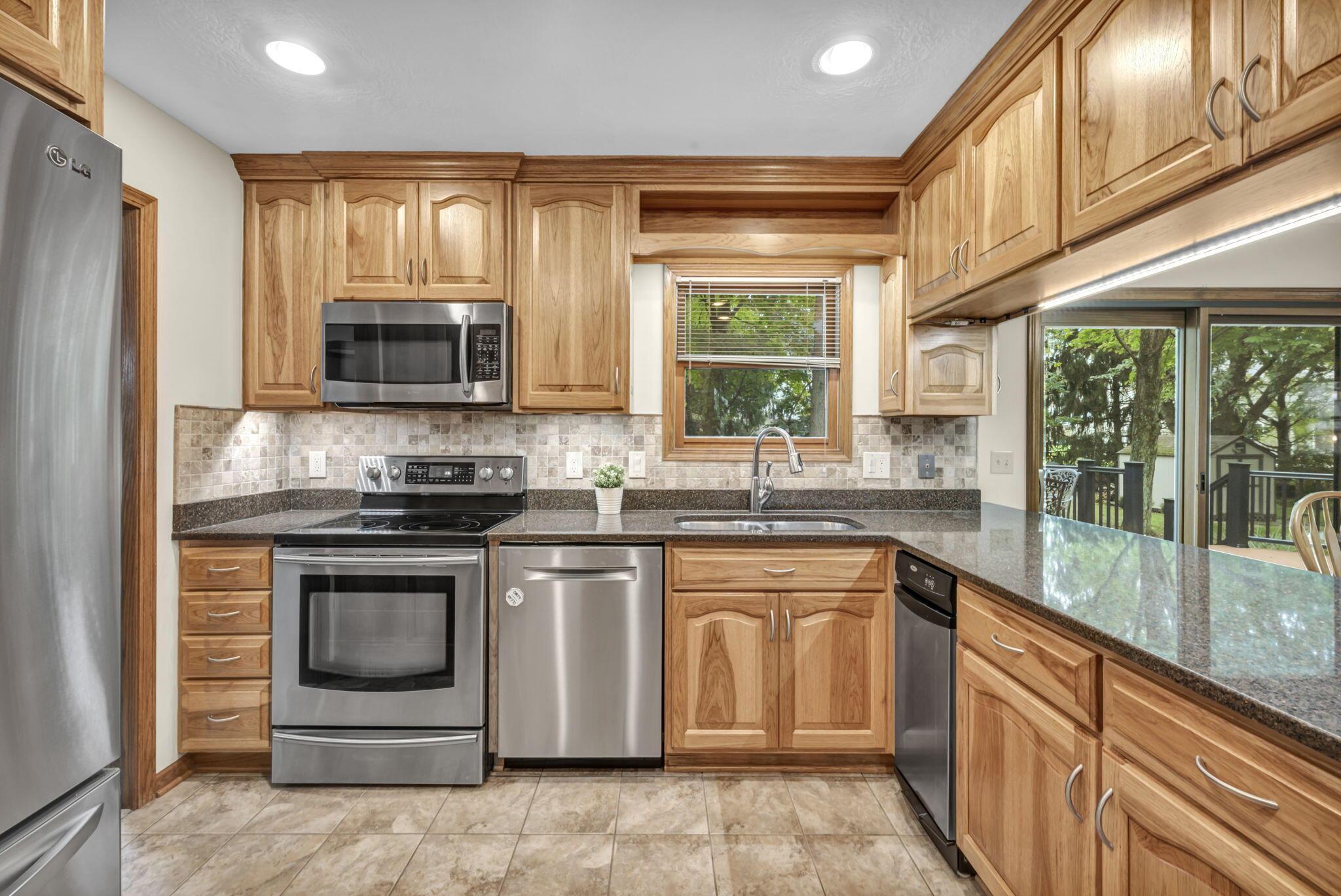 Kitchen with honey-colored wood cabinets, stainless steel appliances, and a long counter beside sliding glass doors.