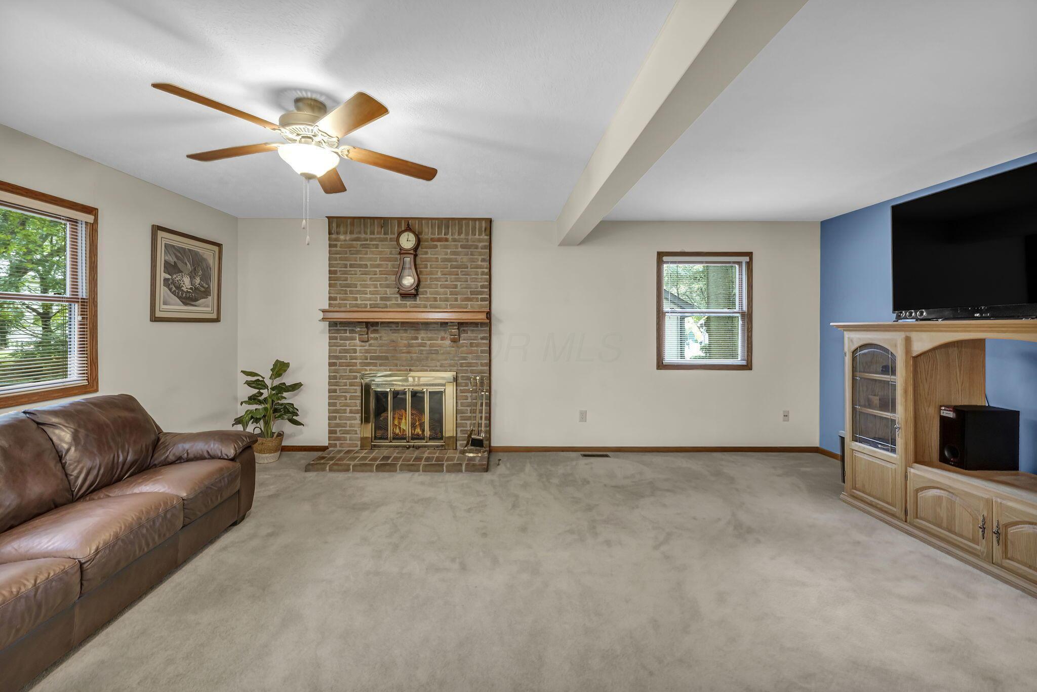 Living room with a brick fireplace, brown leather sofa, and wooden media cabinet.