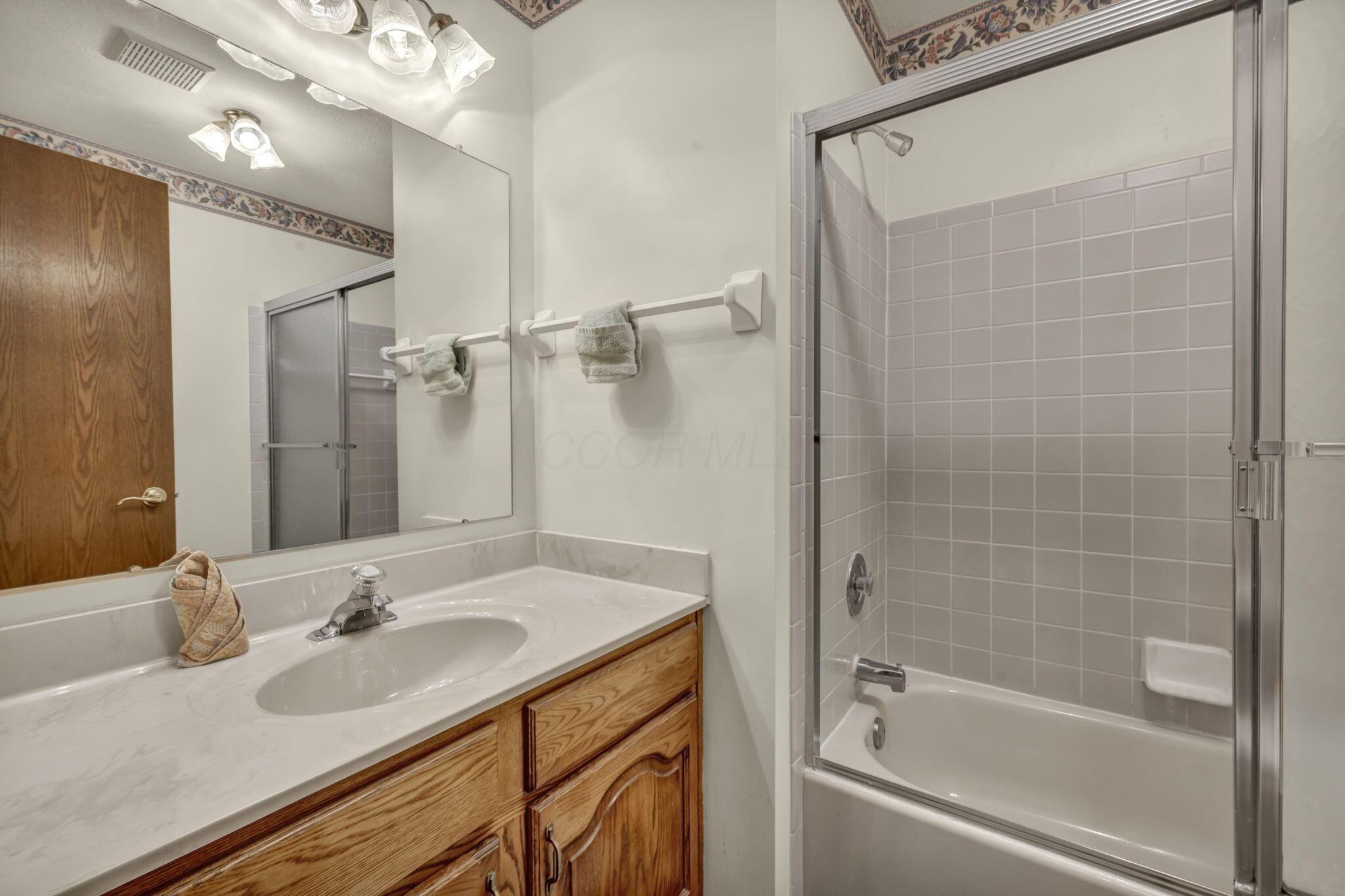 Bathroom with a wood vanity and sink beside a bathtub with sliding glass shower doors.
