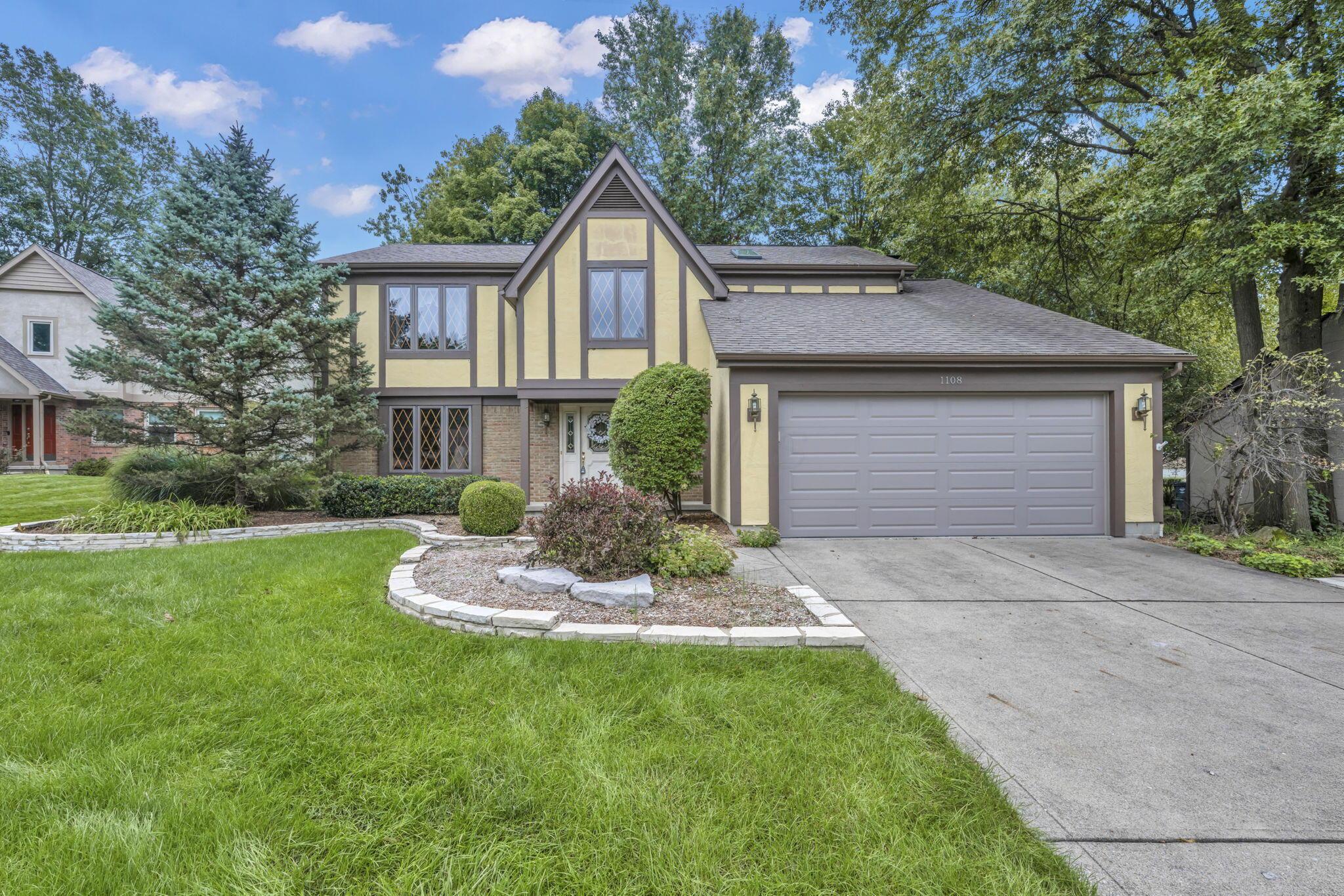 Tudor-style house with a two-car garage, diamond-pane windows, and a curved garden bed.