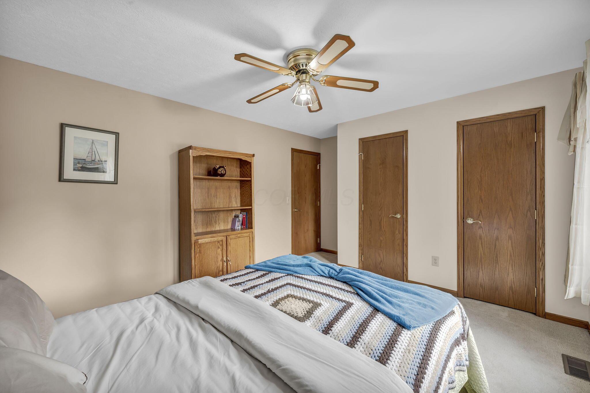 Bedroom with a crocheted quilt, blue blanket, wooden bookcase, and ceiling fan.