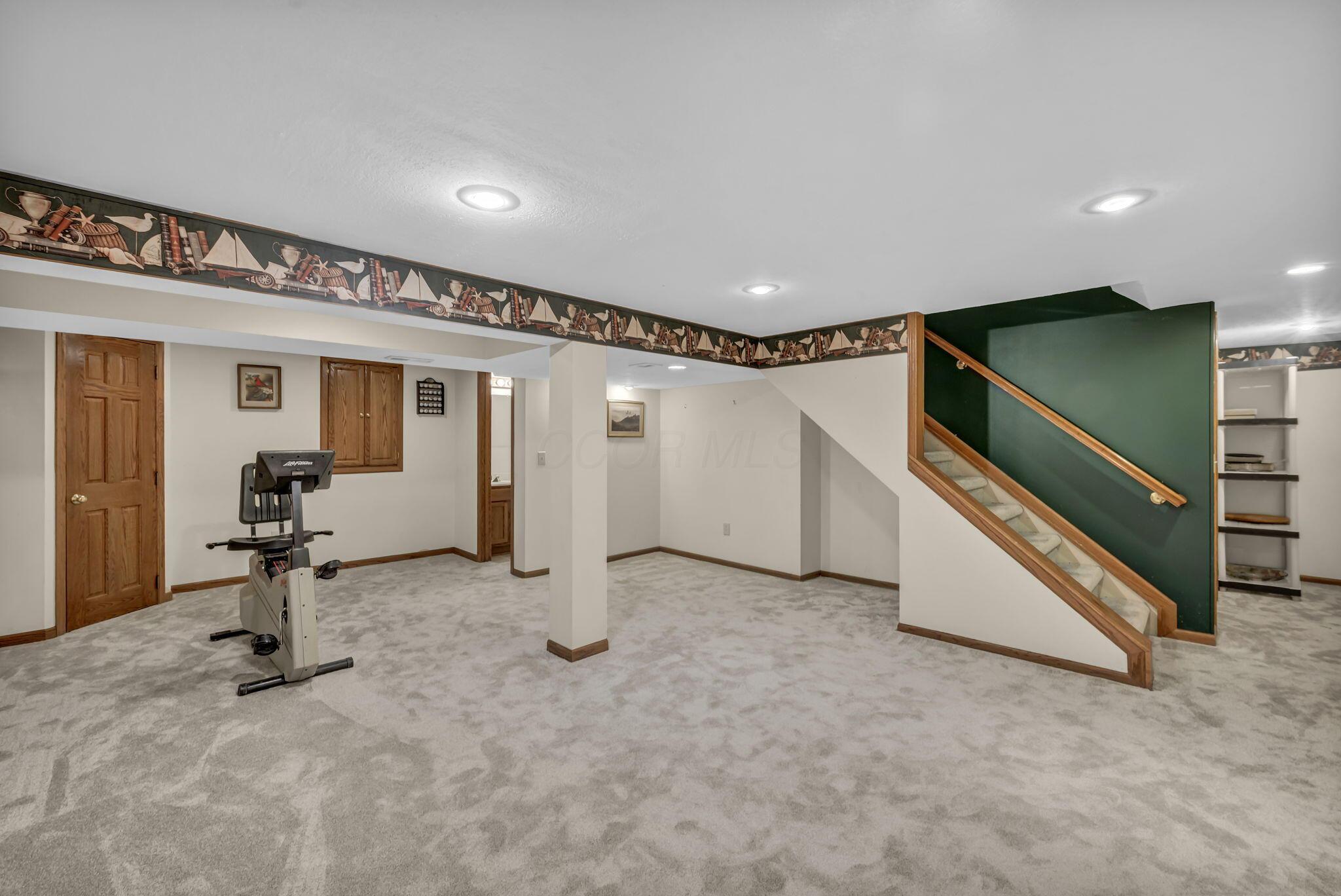 Finished basement with an exercise bike and carpeted stairs beside a dark green accent wall.