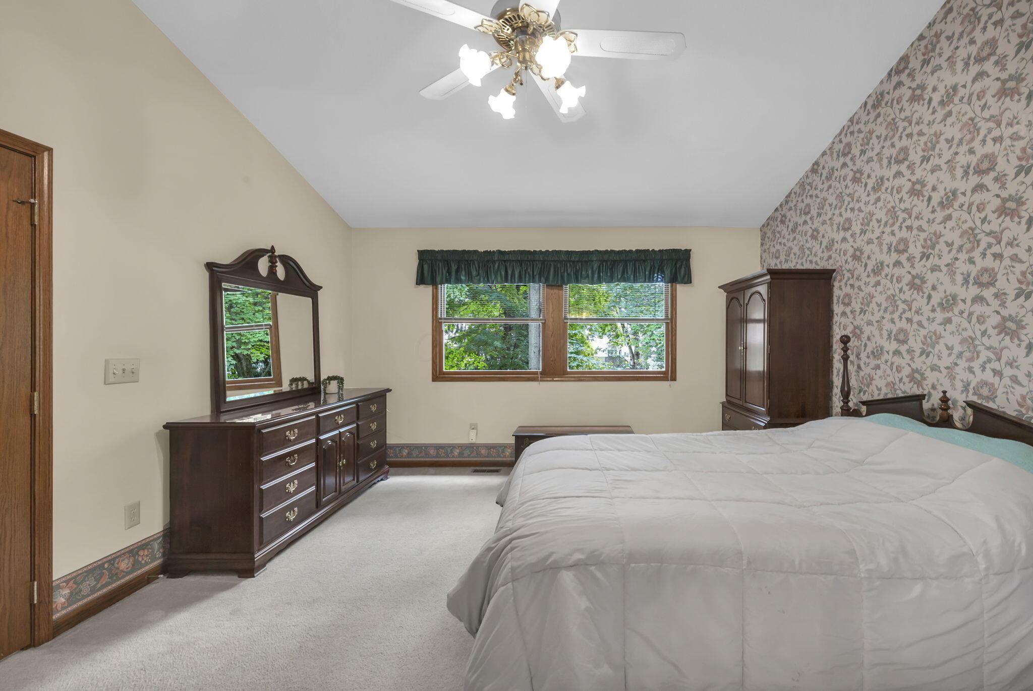 Bedroom with a large bed, dark wood furniture, floral wallpaper, and a window overlooking trees.