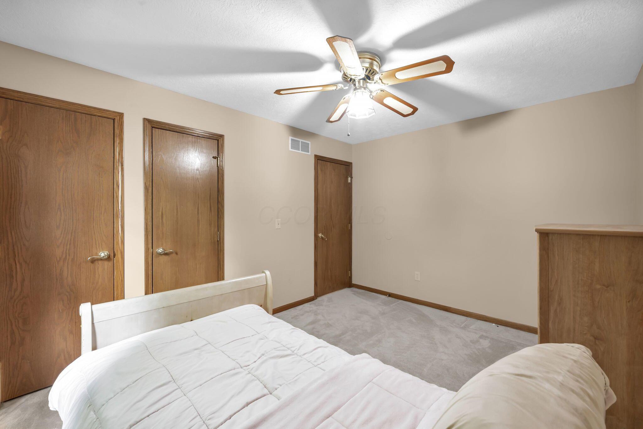 Bedroom with a white bed, three wood doors, carpet, and a ceiling fan with light.