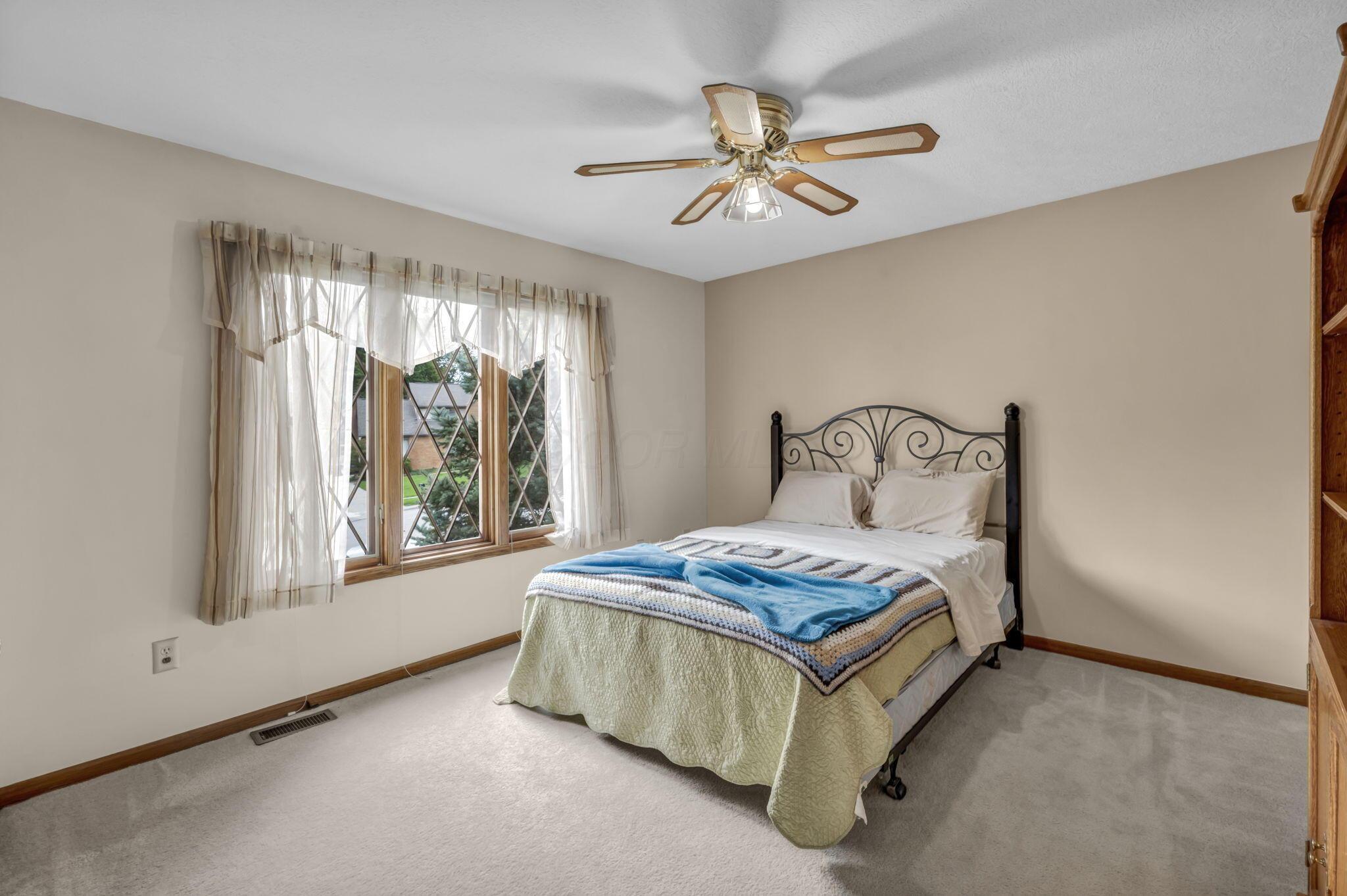 Bedroom with a black metal bed, blue throw, sheer-curtained window, and ceiling fan.