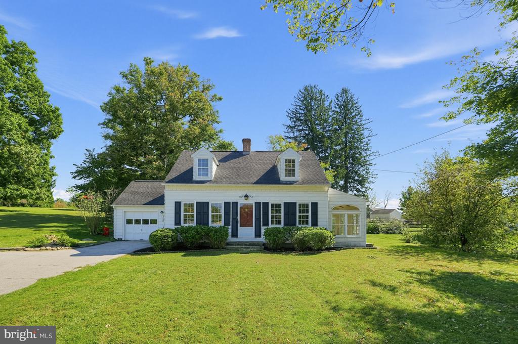 White Cape Cod home with dark shutters, roof dormers, an attached garage, and a broad green lawn.