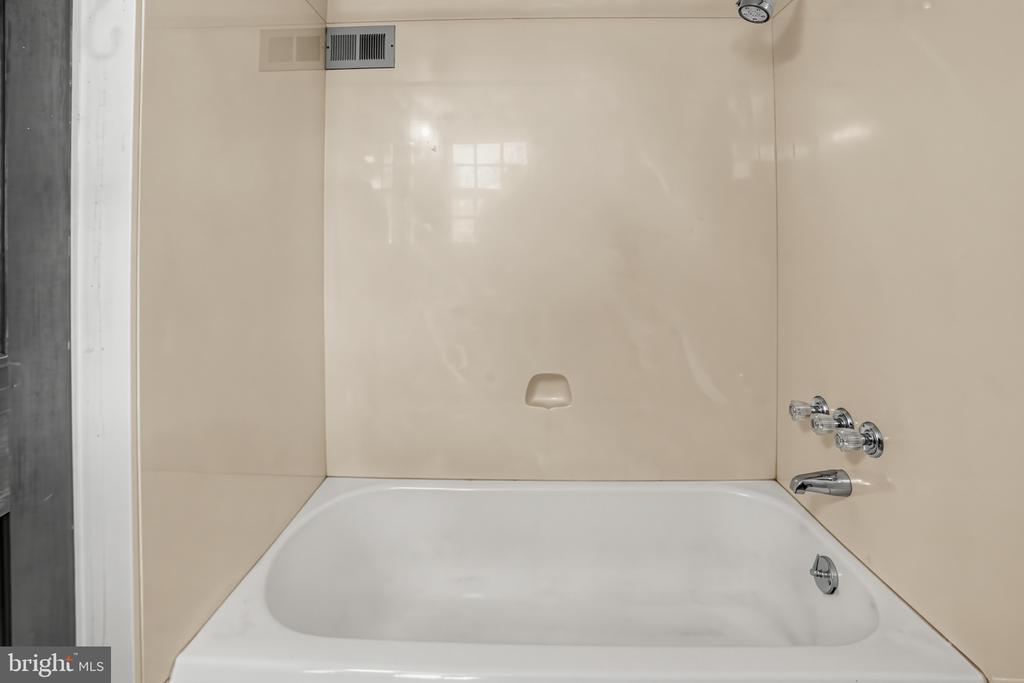 Bathroom bathtub with beige wall panels and chrome faucet controls.