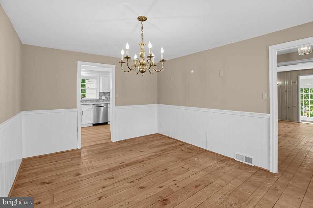 Vacant dining room with wide-plank wood floors, white wainscoting, and a brass chandelier.