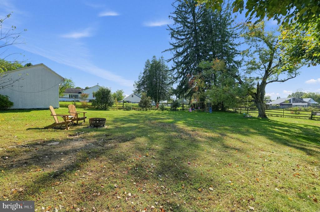 Backyard with a grassy lawn, mature trees, Adirondack chairs, and a fire pit.