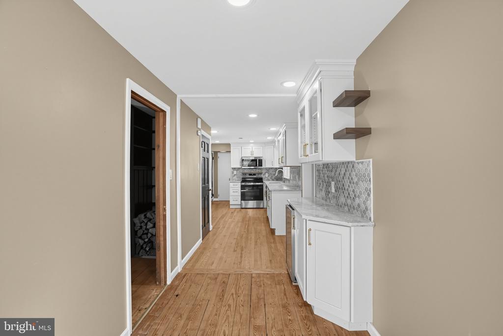 Kitchen with white cabinets, gray patterned backsplash, stainless steel appliances, and wood flooring.